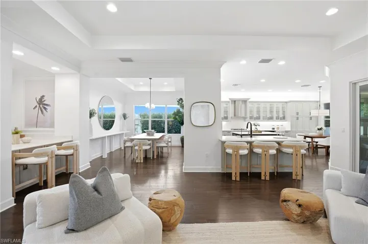 Open-concept living space featuring wood-finish flooring, recessed lighting, crown molding, a kitchen island with a built-in sink, and tray ceilings