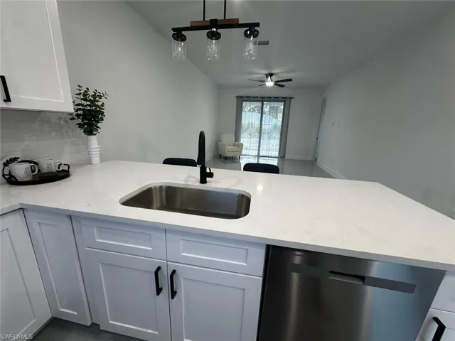 Kitchen island featuring a stainless steel sink with a matte black faucet, light-toned countertop, and white shaker-style cabinetry with black hardware