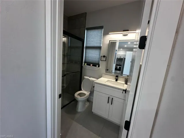 Contemporary bathroom featuring a frameless glass shower enclosure, a white vanity with double-door cabinetry, a rectangular undermount sink, a dark countertop, and a wall-mounted light fixture