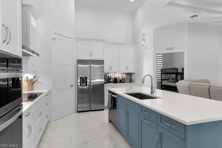 Kitchen with white cabinetry, appliances with stainless steel finishes, light marble finish floors, light stone countertops, and a towering ceiling