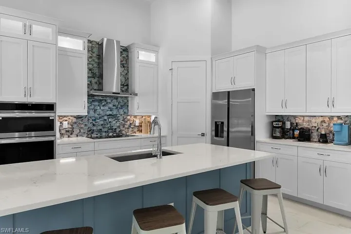 Kitchen with decorative backsplash, white cabinetry, stainless steel appliances, and a kitchen breakfast bar