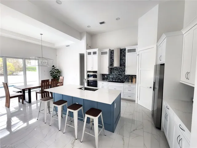 Kitchen with pendant lighting, white cabinetry, a kitchen island with sink, tasteful backsplash, and wall chimney range hood