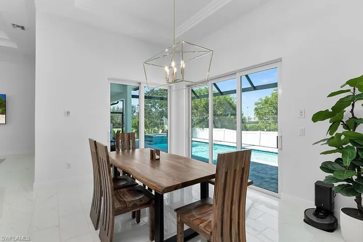 Dining space with light marble finish floors, plenty of natural light, ornamental molding, and a chandelier
