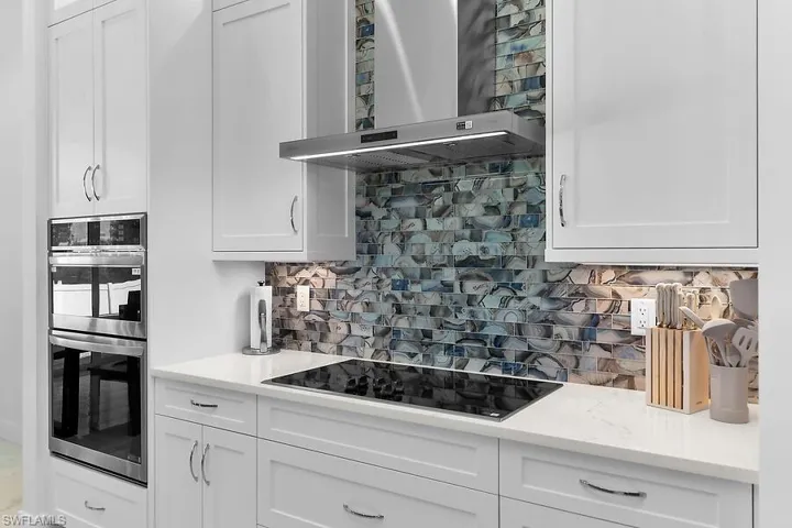Kitchen with backsplash, white cabinets, wall chimney exhaust hood, stainless steel double oven, and black electric cooktop