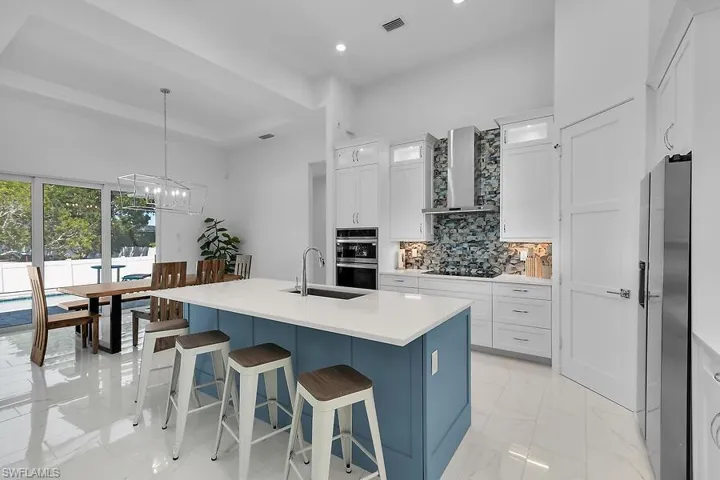Kitchen with blue cabinetry, an island with sink, hanging light fixtures, decorative backsplash, and recessed lighting