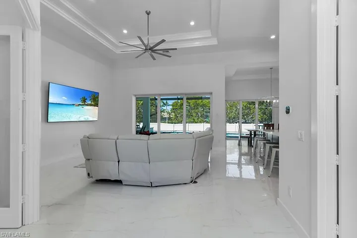 Living room view from front entry featuring a raised ceiling, light marble finish flooring, recessed lighting, crown molding, and a ceiling fan