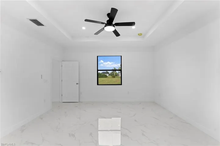 Spare room with light marble finish flooring, a tray ceiling, recessed lighting, and ceiling fan