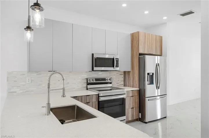 Dual tone kitchen featuring stainless steel appliances, modern cabinets, light stone countertops, hanging light fixtures, and two tone color scheme
