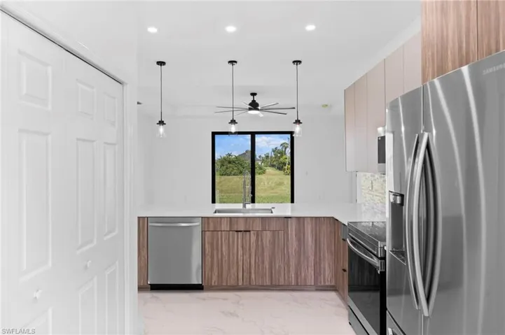 Kitchen featuring stainless steel appliances, wood finish cabinets, modern cabinets, light stone countertops, and a ceiling fan