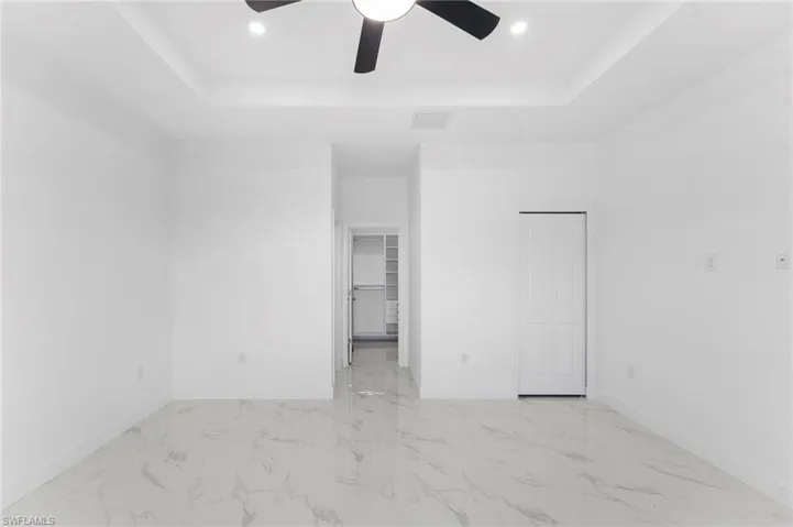 Unfurnished bedroom featuring a closet, a raised ceiling, light marble finish floors, and ceiling fan