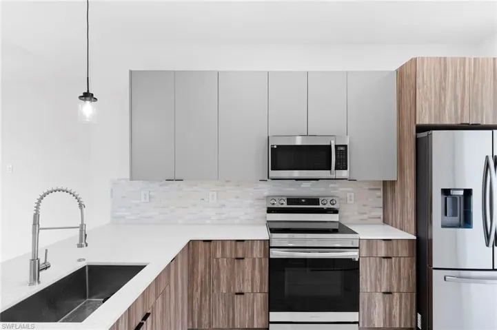 Two tone kitchen featuring stainless steel appliances, modern cabinets, pendant lighting, light stone countertops, and tasteful backsplash