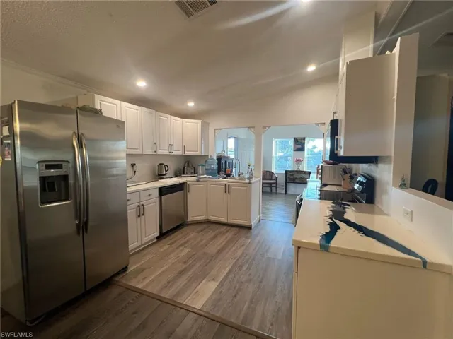 Kitchen featuring appliances with stainless steel finishes, vaulted ceiling, white cabinetry, dark wood-style floors, and recessed lighting