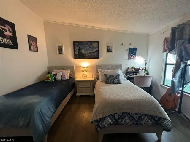 Bedroom with ornamental molding, dark wood finished floors, a textured ceiling, and a textured wall