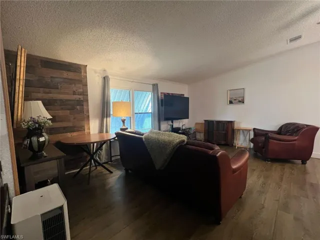 Living area featuring a textured ceiling, wood finished floors, heating unit, wood walls, and lofted ceiling