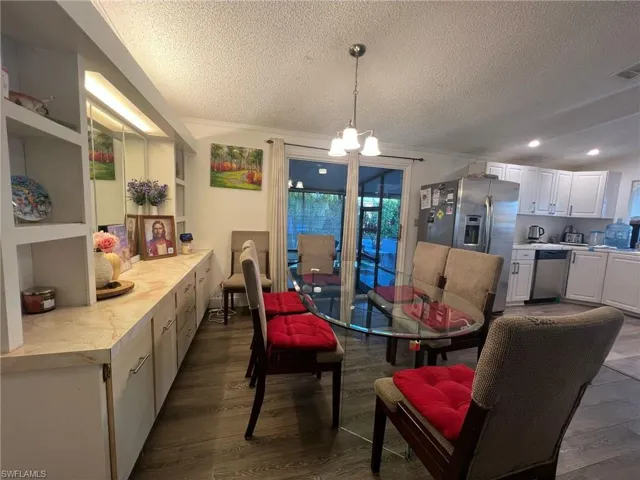 Dining room with dark wood-style floors, a textured ceiling, a chandelier, and ornamental molding