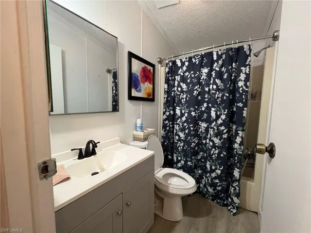 Bathroom featuring a textured ceiling, shower / bath combo, vanity, and light wood finished floors