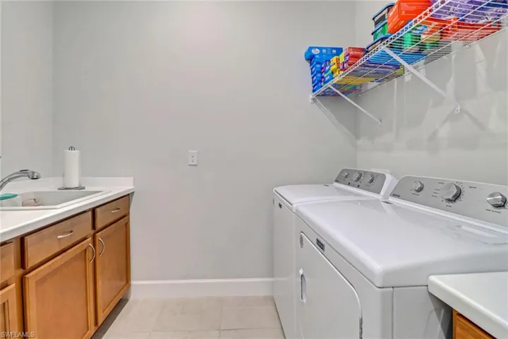 Laundry area with light tile patterned floors, cabinet space, a sink, washer and dryer, and baseboards