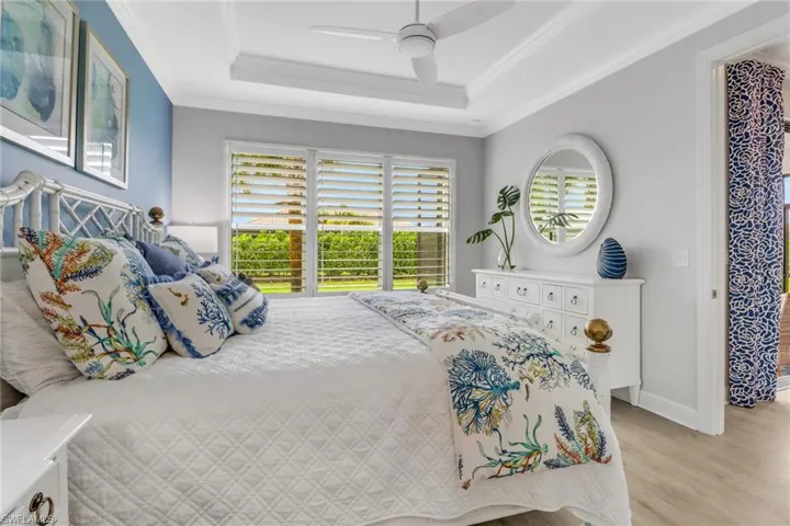 Bedroom with crown molding, a raised ceiling, light wood-style floors, ceiling fan, and baseboards