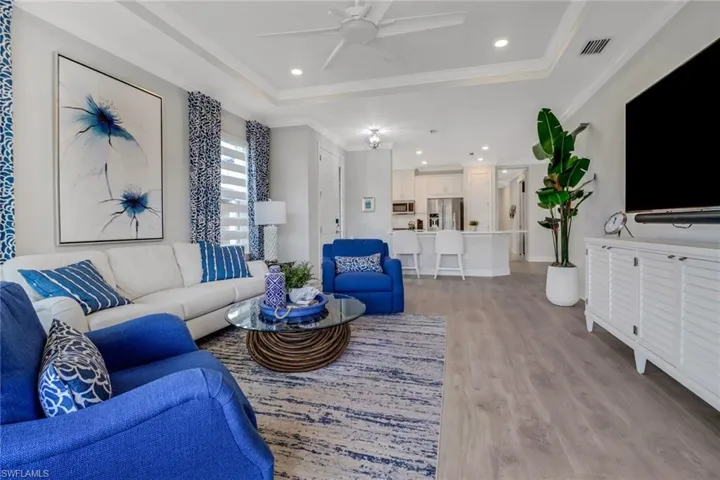 Living room with a tray ceiling, crown molding, light wood finished floors, visible vents, and ceiling fan