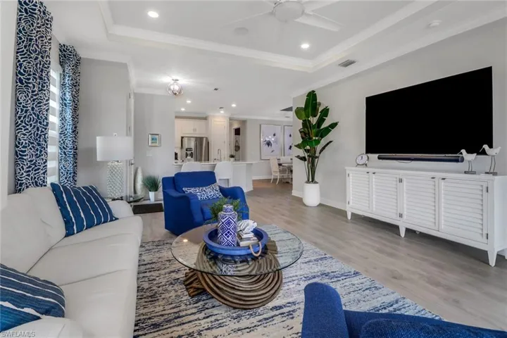 Living room with crown molding, a raised ceiling, a ceiling fan, and light wood-style floors