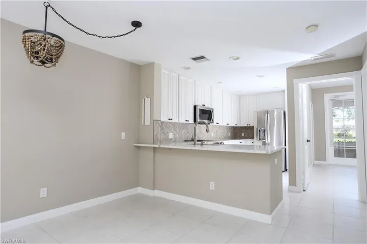 Kitchen featuring tasteful backsplash, white cabinets, light stone counters, a peninsula, and light tile patterned floors