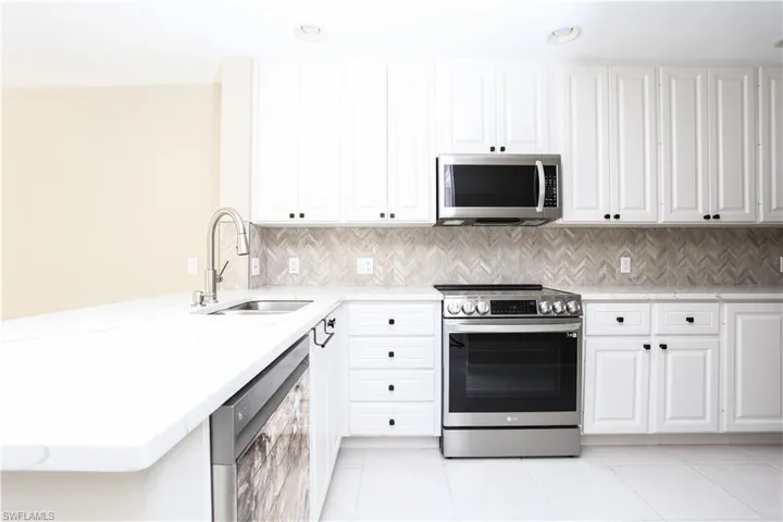 Kitchen with stainless steel appliances, light tile patterned flooring, light stone countertops, and white cabinets