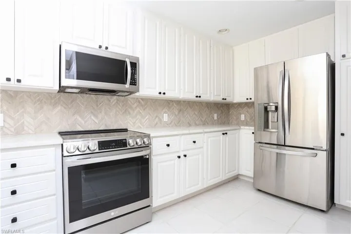 Kitchen featuring stainless steel appliances, decorative backsplash, light tile patterned floors, and white cabinetry