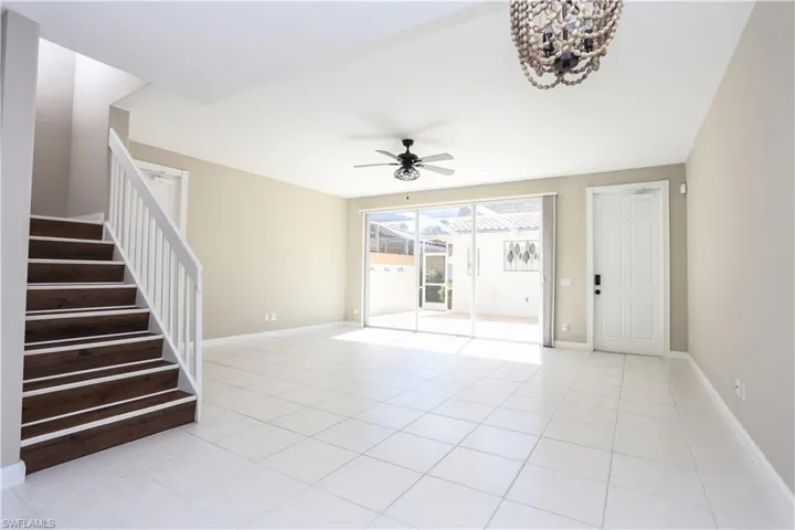 Empty room with light tile patterned floors, ceiling fan, and stairway