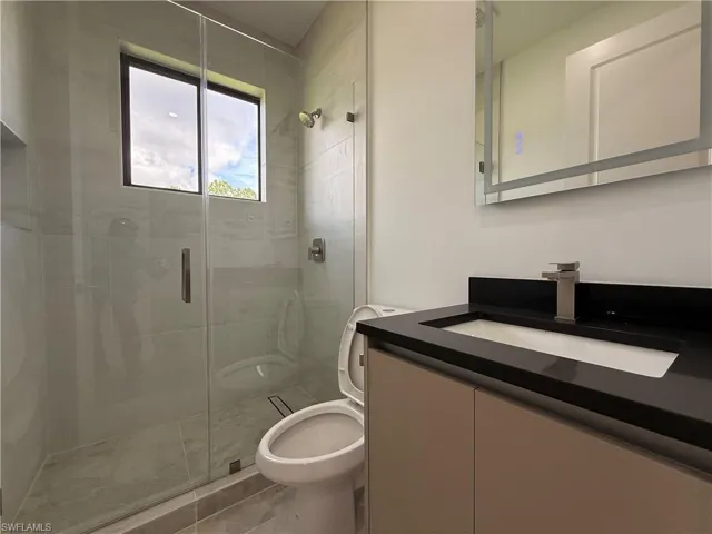 Glass-enclosed shower with a window, single vanity with dark countertop, and an illuminated mirror