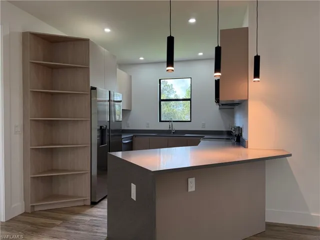 Contemporary kitchen featuring an integrated breakfast bar, stainless steel refrigerator, dark countertops, and pendant lighting