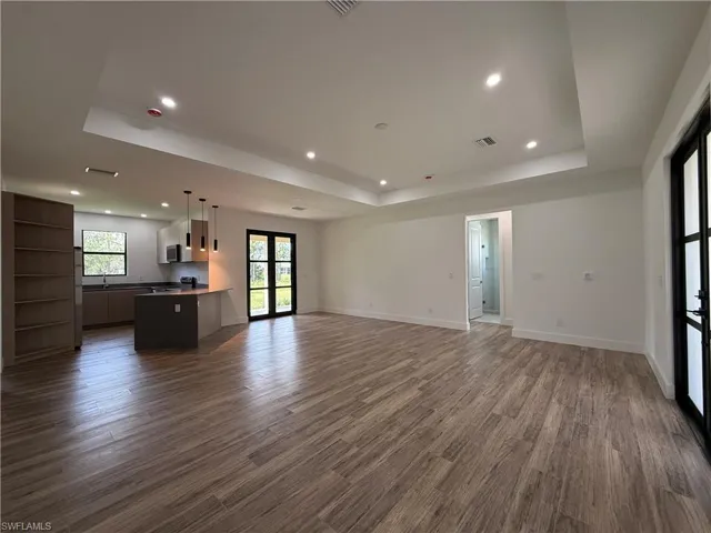 Tray ceiling with recessed lighting, wood-finish flooring, built-in shelving, kitchen island with pendant lighting, and black-framed French doors