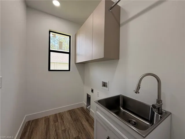 Utility room featuring wood-finish flooring, a utility sink with a brushed nickel faucet, upper cabinetry, and a window