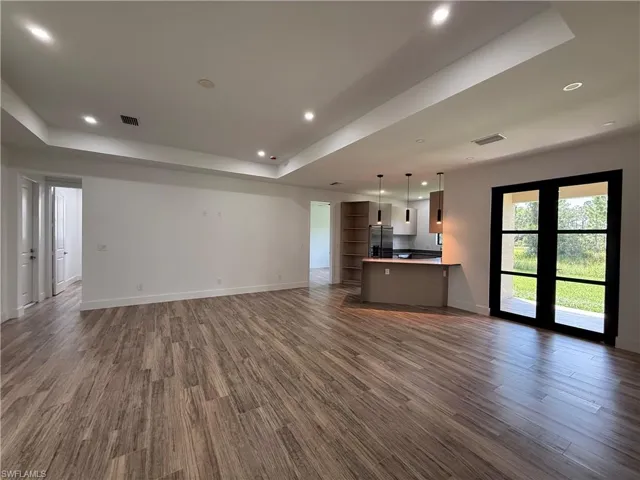 Tray ceiling with recessed lighting, wood-finish flooring, two-panel interior doors, black-framed French doors, and a built-in kitchen island with pendant lighting