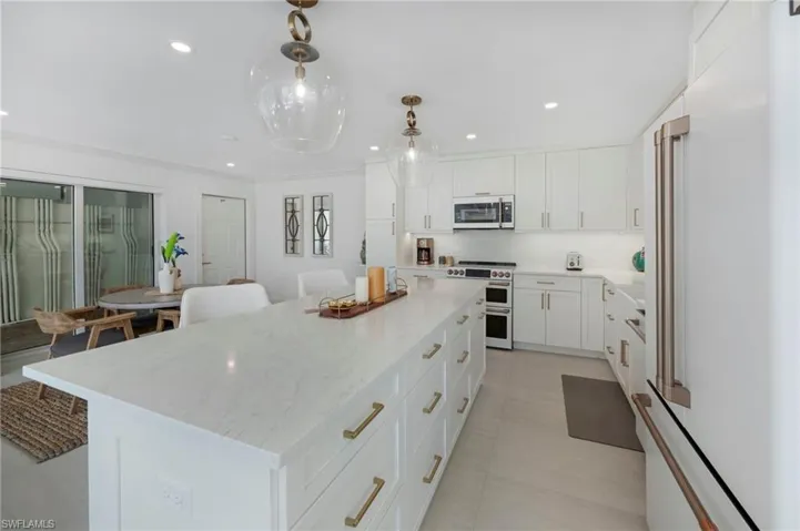 Kitchen with premium appliances, decorative light fixtures, light stone counters, and a kitchen island