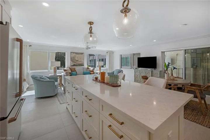 Kitchen featuring white cabinetry, light tile patterned flooring, hanging light fixtures, light stone counters, and stainless steel refrigerator