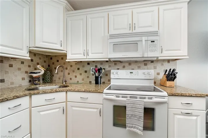 Kitchen with white appliances, white cabinetry, light stone countertops, and decorative backsplash