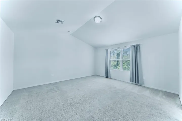 Carpeted empty room with vaulted ceiling and baseboards