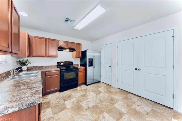 Kitchen with black range with electric stovetop, stainless steel fridge with ice dispenser, brown cabinets, and under cabinet range hood