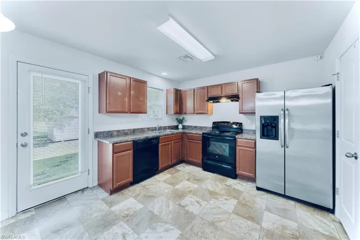 Kitchen featuring black appliances, dark countertops, under cabinet range hood, brown cabinets, and stone finish floors