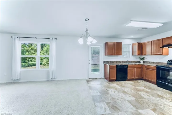 Kitchen with black appliances, a chandelier, decorative light fixtures, brown cabinetry, and under cabinet range hood