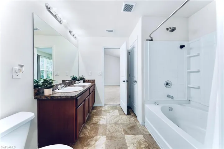 Full bath featuring double vanity, shower / tub combo with curtain, and stone finish flooring
