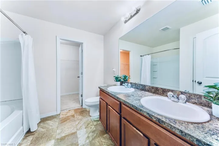 Bathroom featuring double vanity, a spacious closet, and shower / bath combo with shower curtain