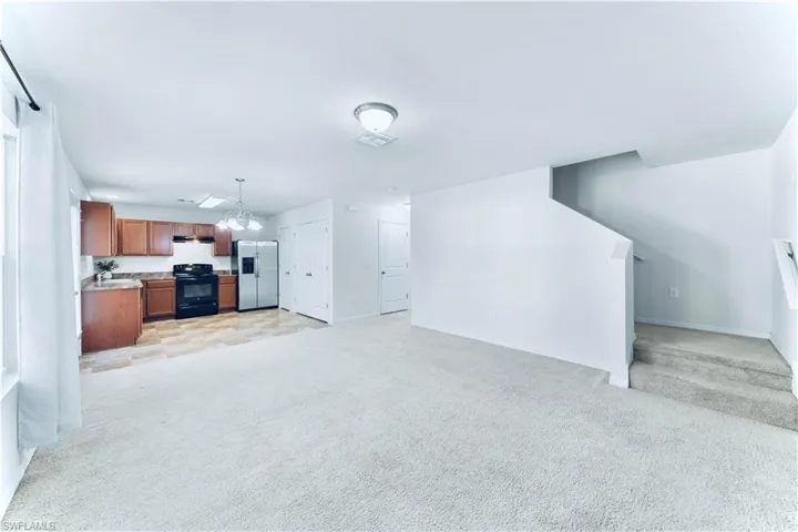 Unfurnished living room with light carpet, a chandelier, and stairway