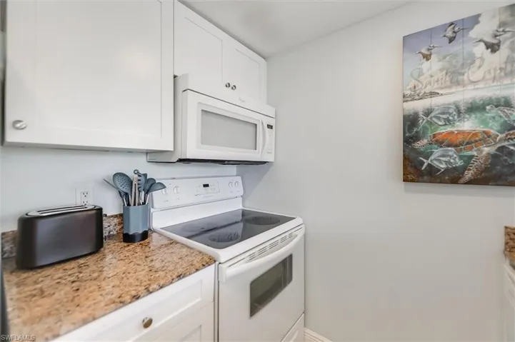 Kitchen featuring white appliances, white cabinets, and light stone counters