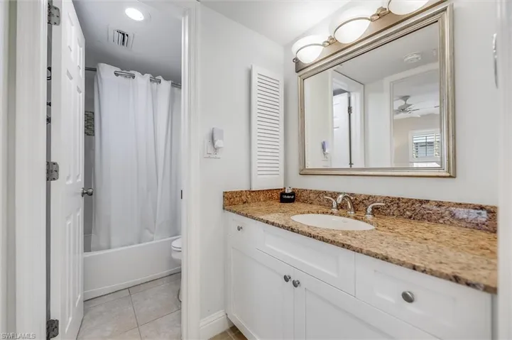 Bathroom with shower / bath combo with shower curtain, light tile patterned floors, and vanity