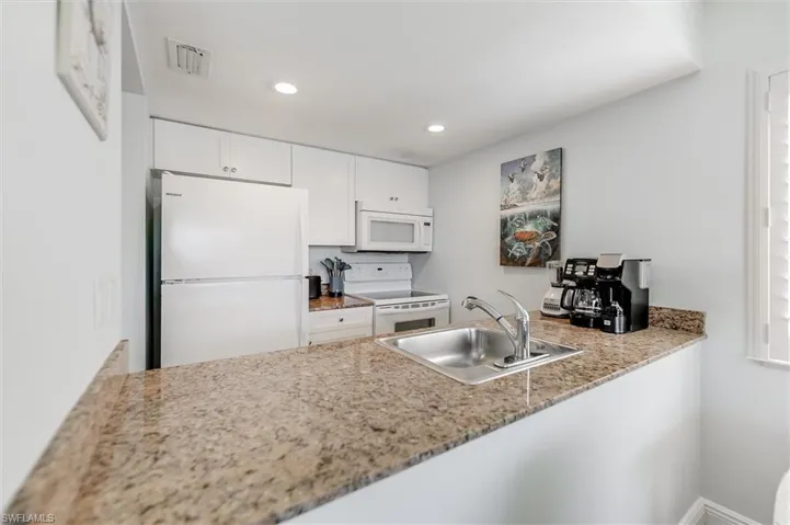 Kitchen with white appliances, white cabinetry, recessed lighting, light stone counters, and a peninsula