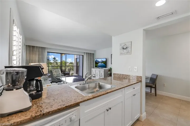 Kitchen featuring white cabinetry, white dishwasher, light tile patterned floors, and light stone countertops