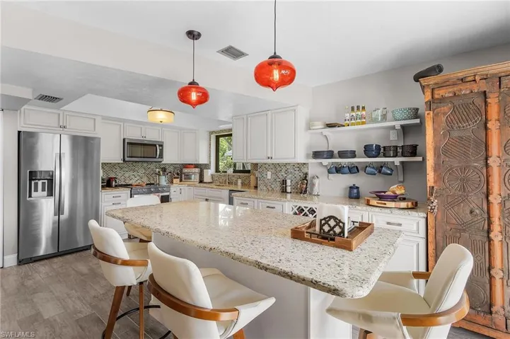 Kitchen featuring stainless steel appliances, a kitchen island, decorative backsplash, white cabinets, and light wood-type flooring