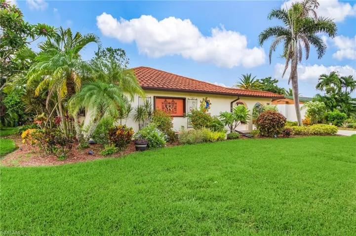 View of front of property with a tile roof, a front lawn, tropical trees,  and stucco siding