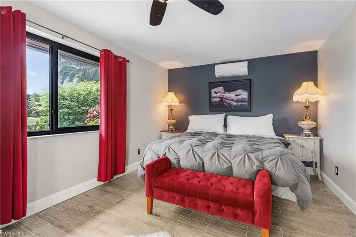 Bedroom with wood finish floors, a wall unit AC, and ceiling fan